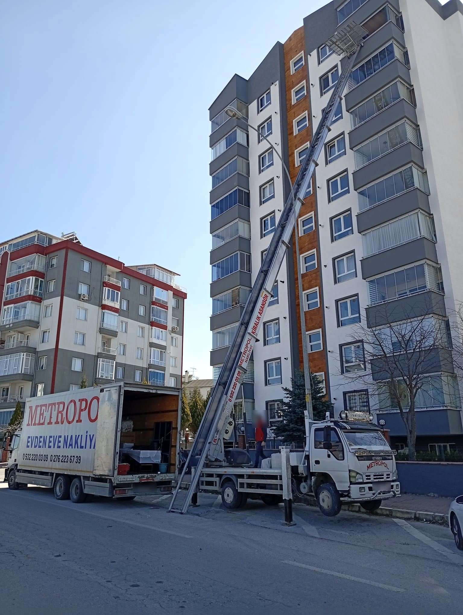 Uşak’ta on katı aşkın bir apartmanın en üst katına uzanan dış cephe asansörü, önünde yüklenen kamyon