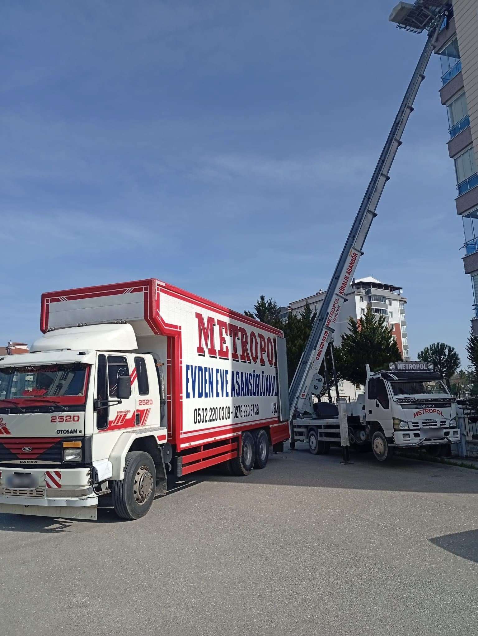 Kırmızı-beyaz Metropol kamyonu ile arkasında yüksek bir binaya açılmış kiralık asansör, açık havada