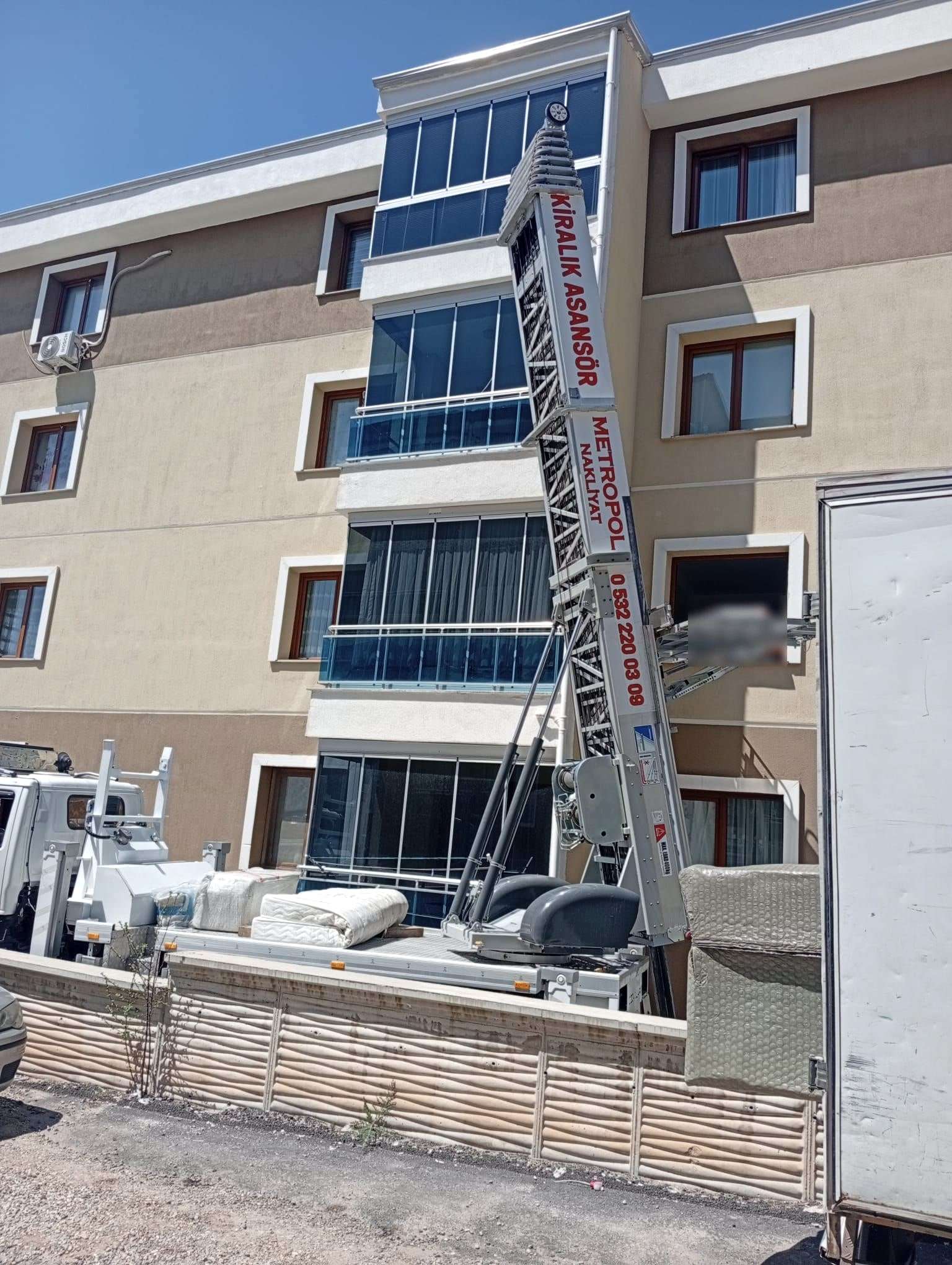 Yakın plan: pencere hizasına dayanmış asansör platformu ve aracın kasasında paketli yatak ve eşyalar