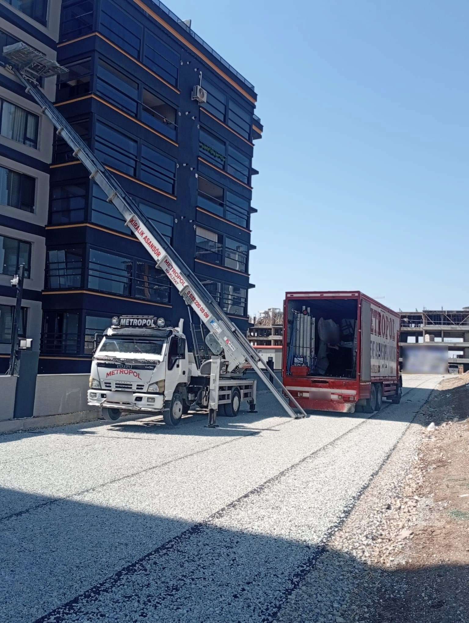 Koyu cepheli yeni bir apartmanın üst katına uzanan asansör ve kapağı açık, içi yüklenmekte olan kırmızı kamyon