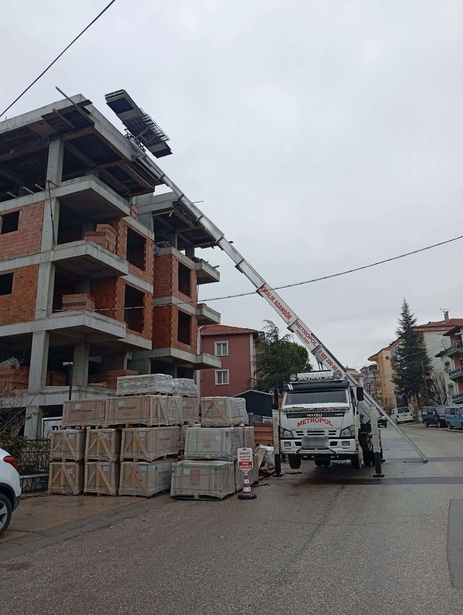 İnşaat hâlindeki bir binanın çatı katına malzeme çıkaran kiralık asansör ve önünde dizili seramik paletleri