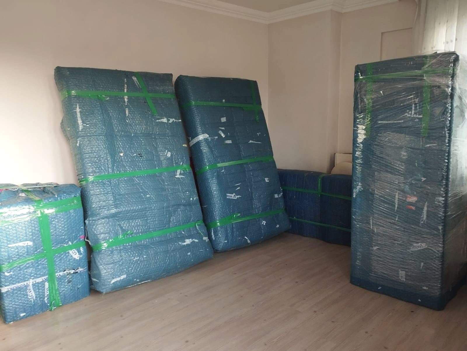 Balonlu naylon ve yeşil bantla paketlenmiş dolap kapakları ve gövdeleri, boş odada taşınmayı bekliyor