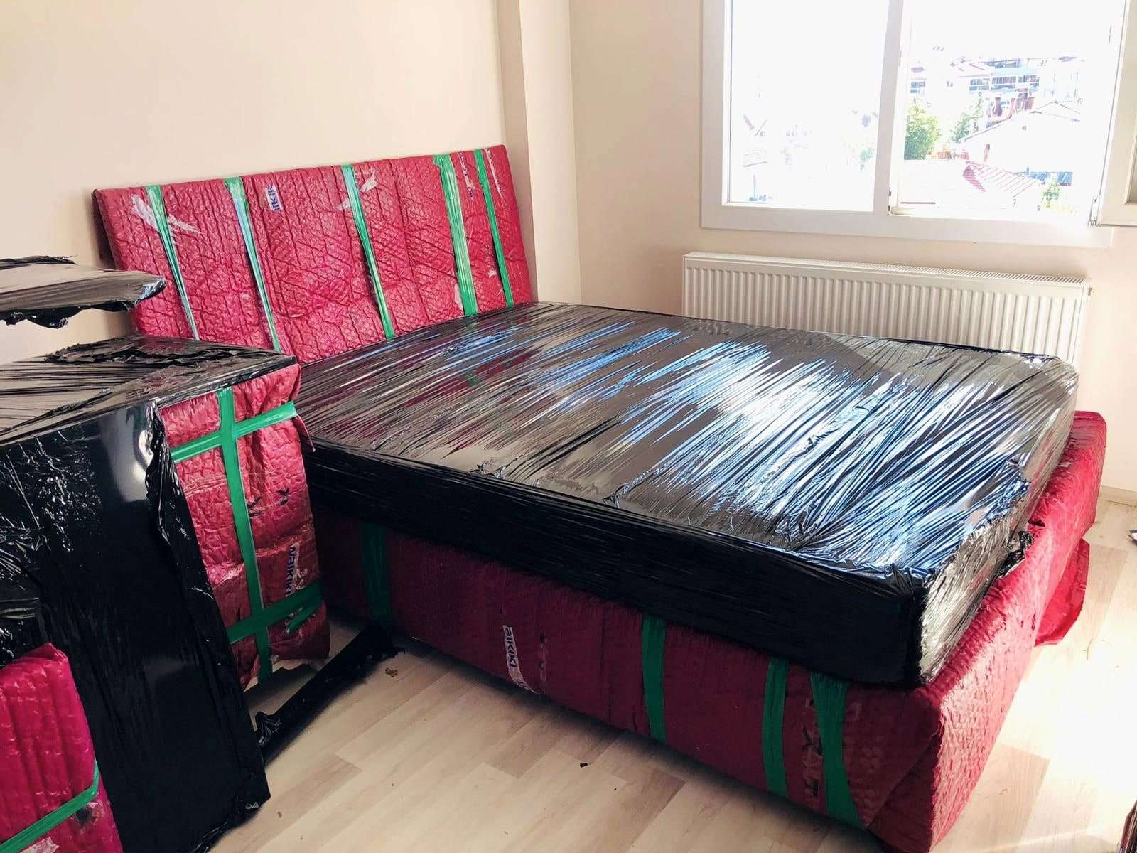 Yatak odasında battaniyeye sarılmış karyola başlığı ve siyah streçle kaplanmış yatak