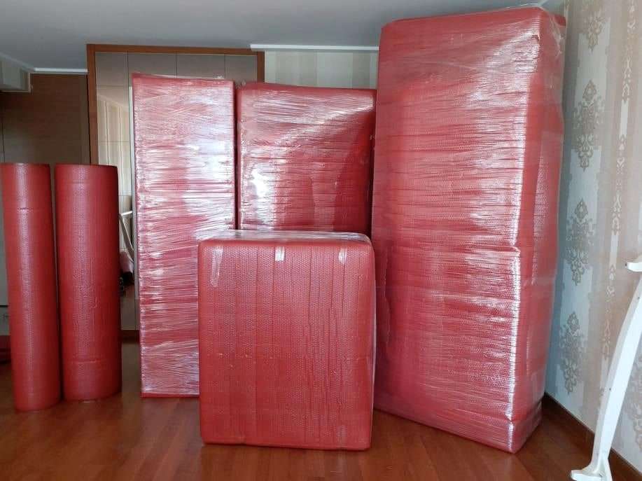 Kırmızı balonlu naylonla paketlenmiş gardırop parçaları ve yanda rulo hâlinde ambalaj malzemesi