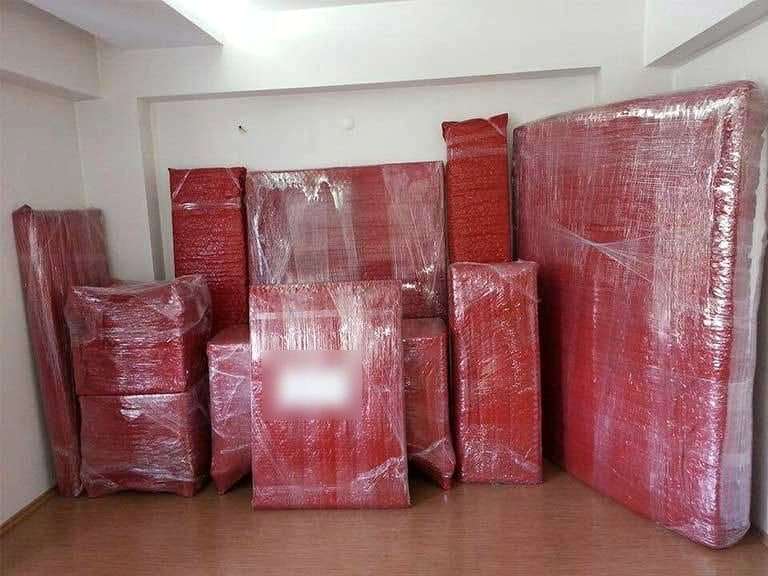 Kırmızı balonlu naylonla paketlenmiş yatak, karyola parçaları ve koliler duvar boyunca