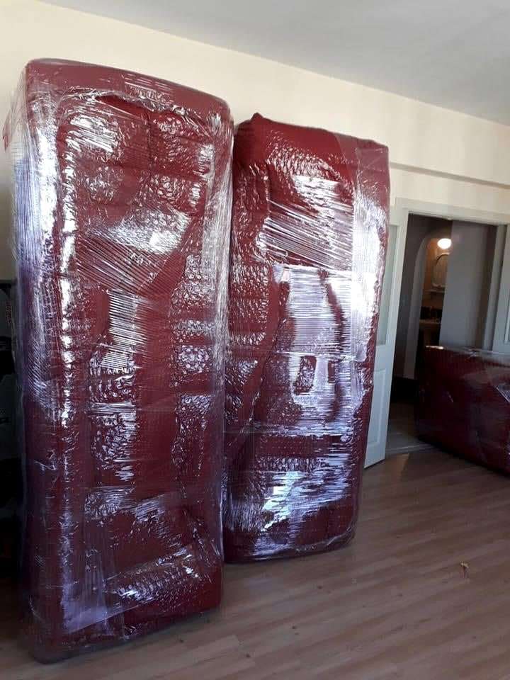 Bordo battaniye ve streçle dik olarak paketlenmiş iki büyük dolap, kapı önünde