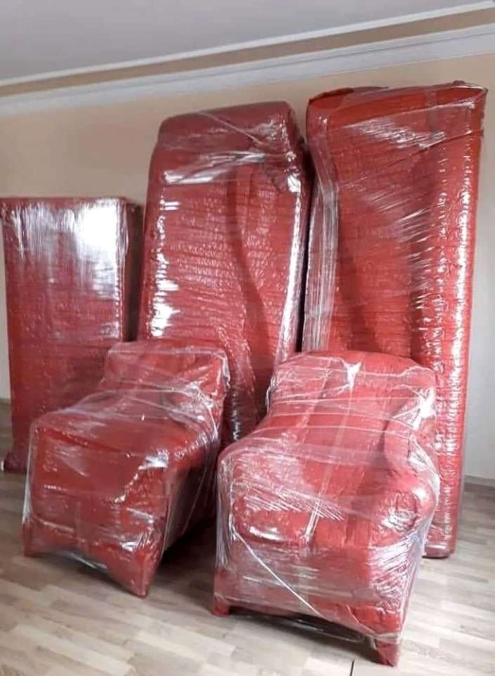Kırmızı ambalajla sarılmış iki tekli koltuk ve arkalarında paketlenmiş uzun mobilyalar