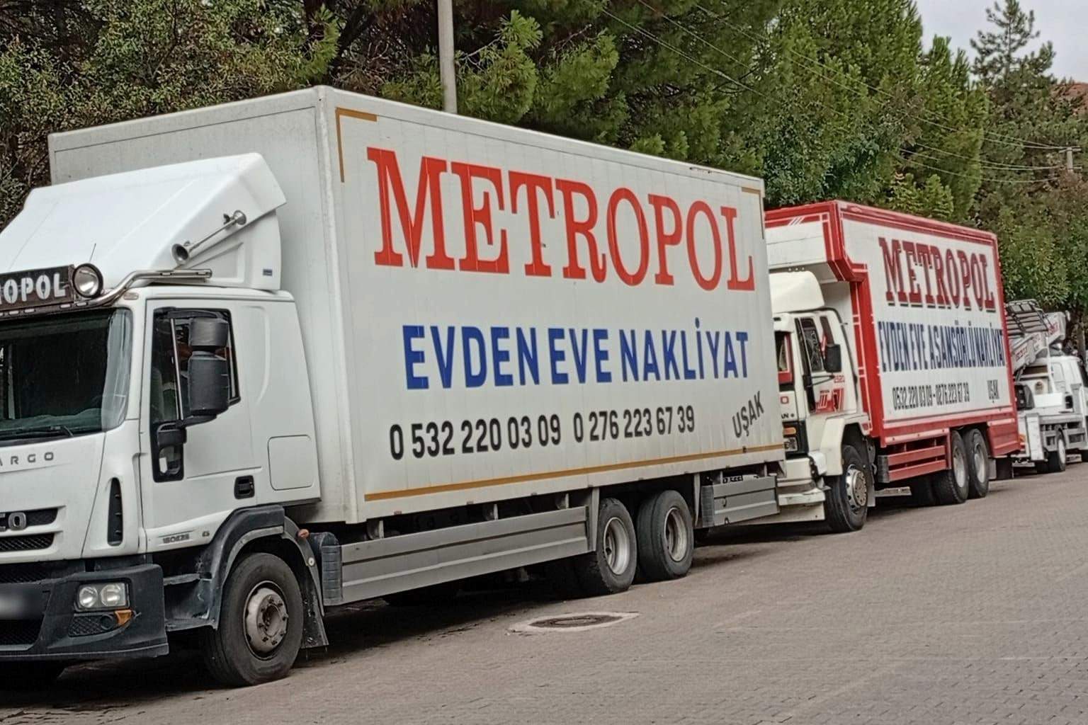 Yan yana park etmiş, üzerinde Metropol, Evden Eve Nakliyat ve Uşak yazan kapalı kasa kamyonlar