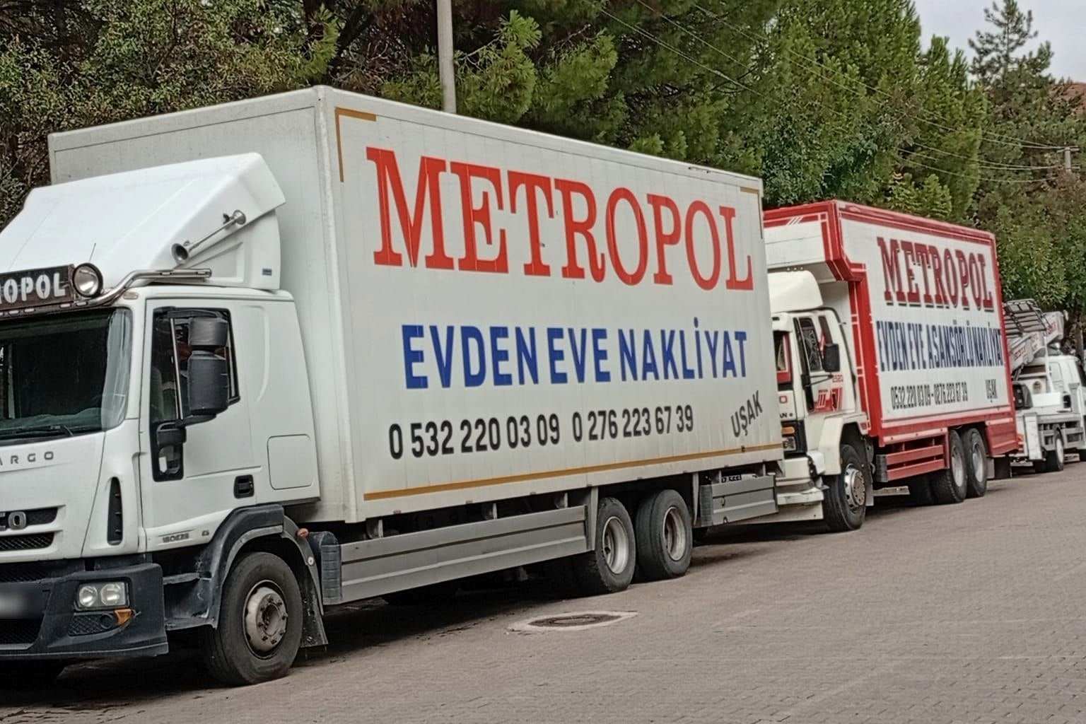 Yan yana park etmiş, üzerinde Metropol, Evden Eve Nakliyat ve Uşak yazan kapalı kasa kamyonlar