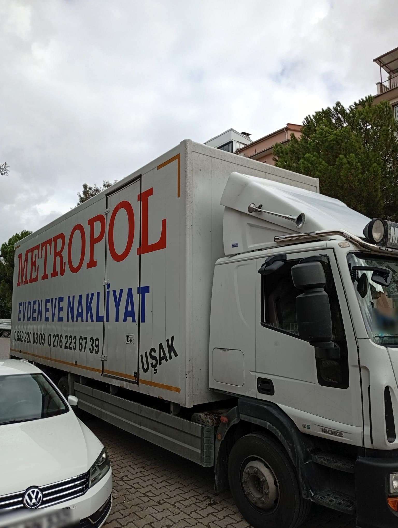 Üzerinde Uşak yazan beyaz kapalı kasa Metropol kamyonu, yan kapısı ve telefon numaraları görünüyor