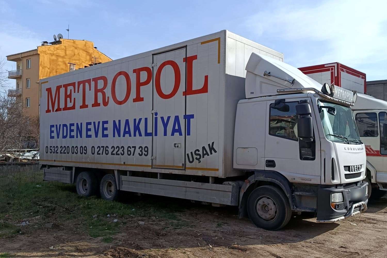 Güneşli bir günde toprak alanda bekleyen Metropol kamyonu ve arkasında kırmızı bir Metropol kamyonu